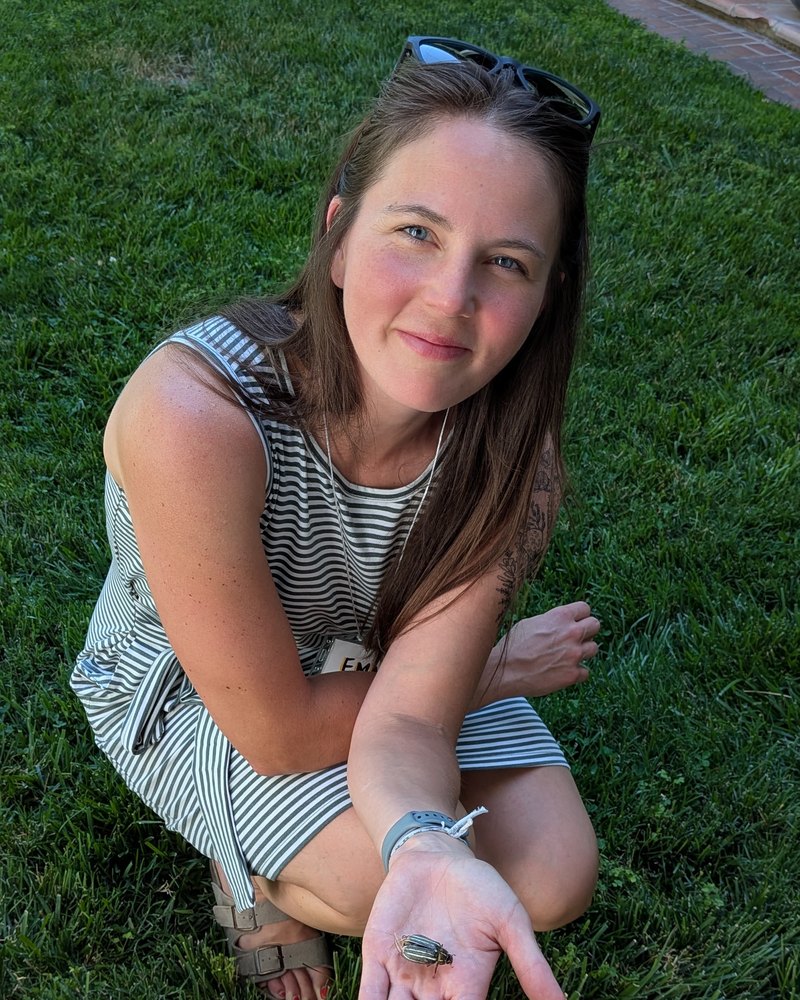 Emma Wellman crouched on the grass, holding a beetle in her palm